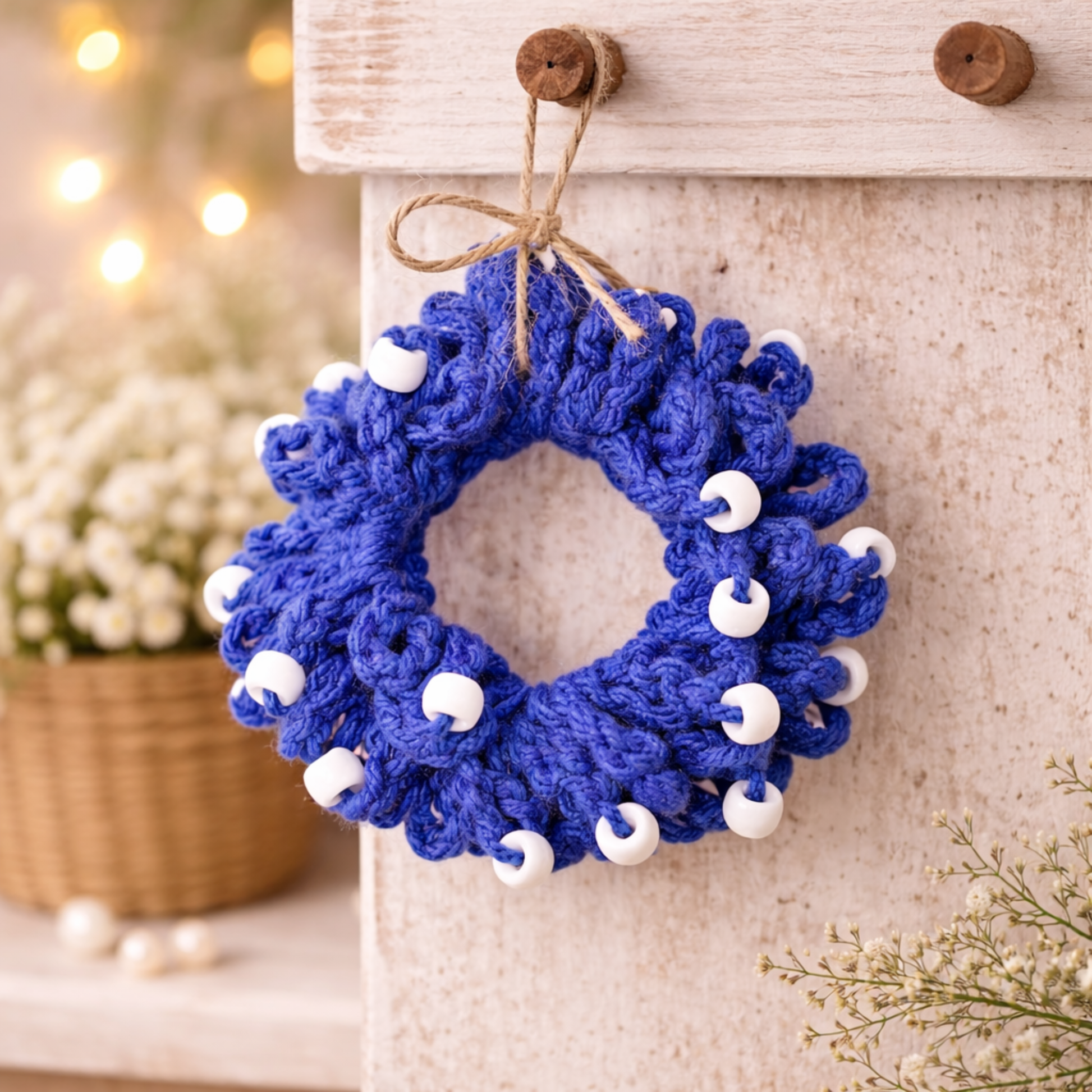 Blue crocheted wreath with white beads hanging on a wooden surface.