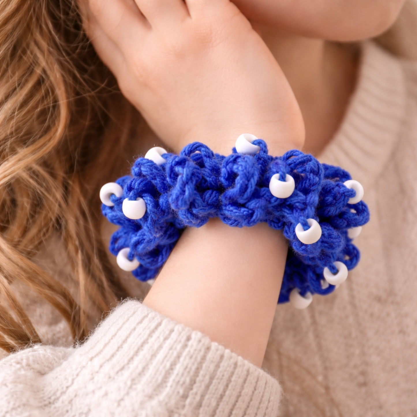 Blue knitted bracelet with white beads on a person's wrist, wearing a beige sweater.