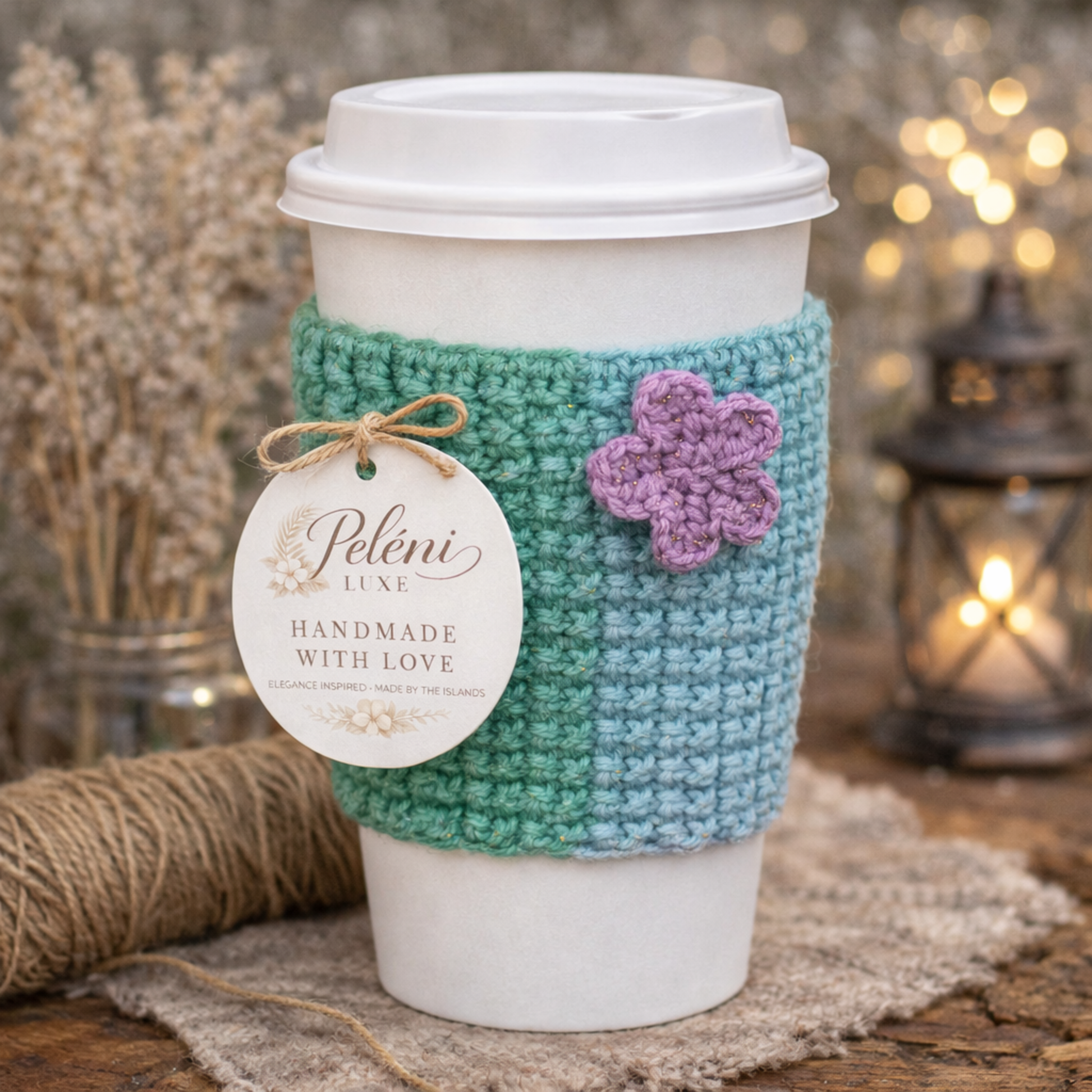 Coffee cup with a green and blue crocheted sleeve and a purple flower, branded 'Peleni Luxe'.